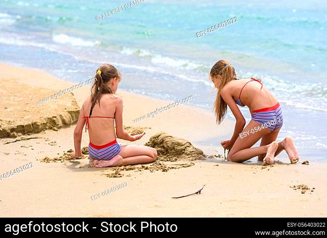 Two girls build sand castles on the seashore, back view
