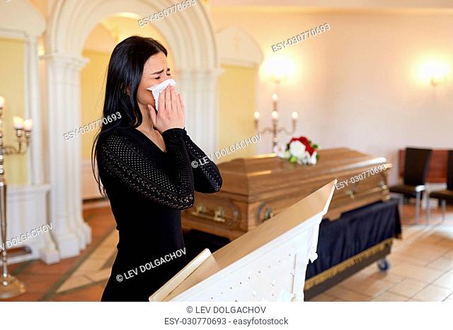 burial, people, grief and mourning concept - close up of sad woman with napkin crying near coffin at funeral in church
