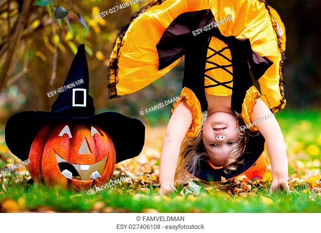 Little girl in witch costume playing in autumn park. Child having fun at Halloween trick or treat. Kids trick or treating