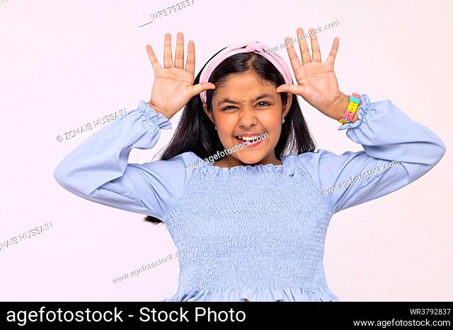 Portrait of little girl making funny face against plain background