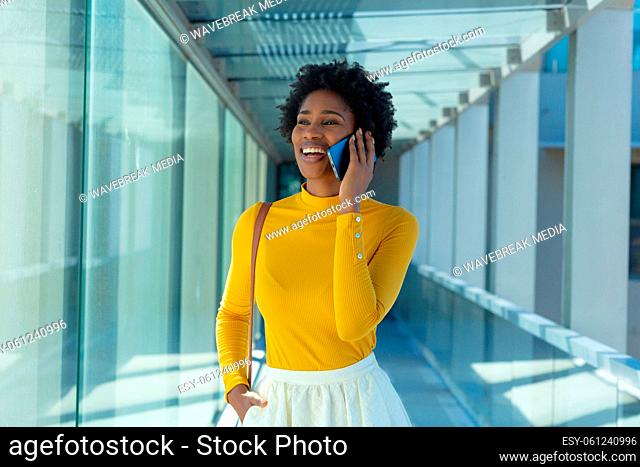 Cheerful young african american businesswoman talking on mobile phone in corridor at workplace