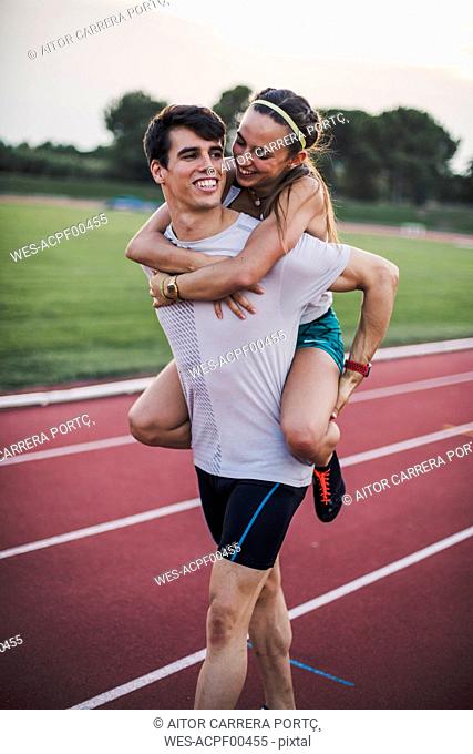 Happy athlete giving his girlfriend a piggyback ride on a tartan track
