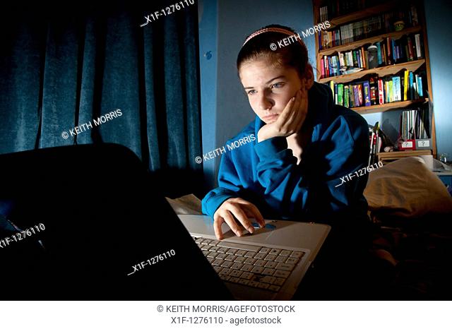 A 16 sixteen year old teenage girl reading Facebook on her laptop in her bedroom at home UK