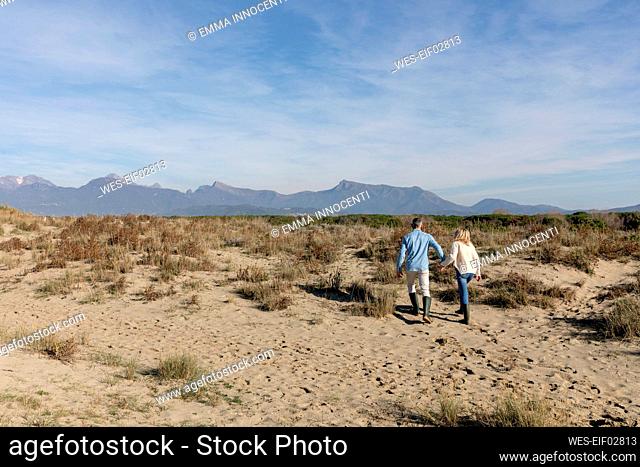 Couple walking together amidst plants on sand at dunes