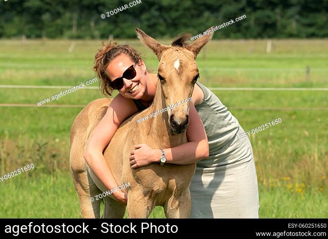Young woman cuddling with her best friend, falcon color stallion foal, sharing love and mutual affection