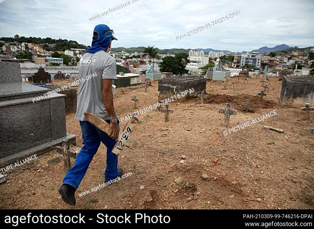 06 March 2021, Brazil, Rio De Janeiro: Douglas Silva, who works at Iraja Cemetery, places a cross with a date on a grave