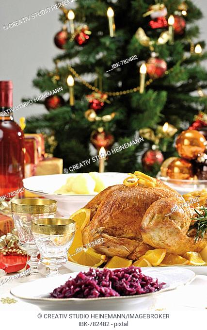 Roast turkey on a festive table setting served with red cabbage and dumplings in front of a decorated Christmas tree