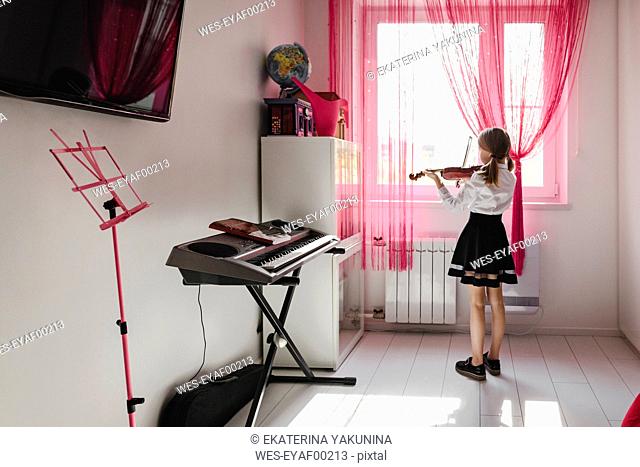 Girl playing violin at the window at home