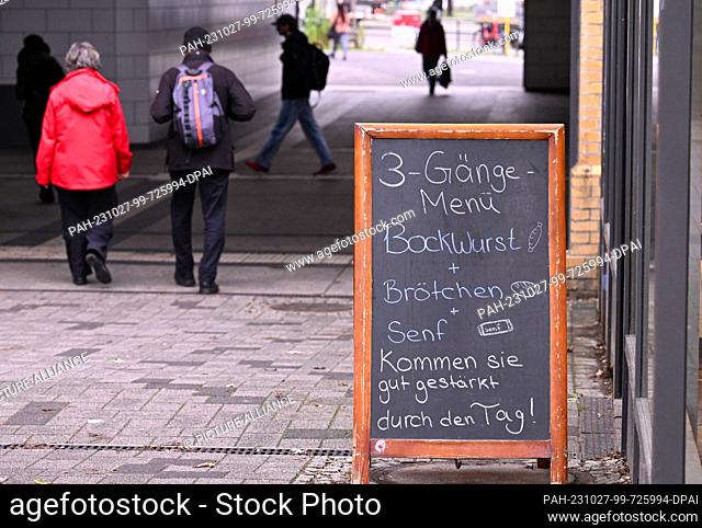 27 October 2023, Berlin: Passers-by walk past a sign in front of a bakery in the S-Bahn underpass, on which the combination of bockwurst