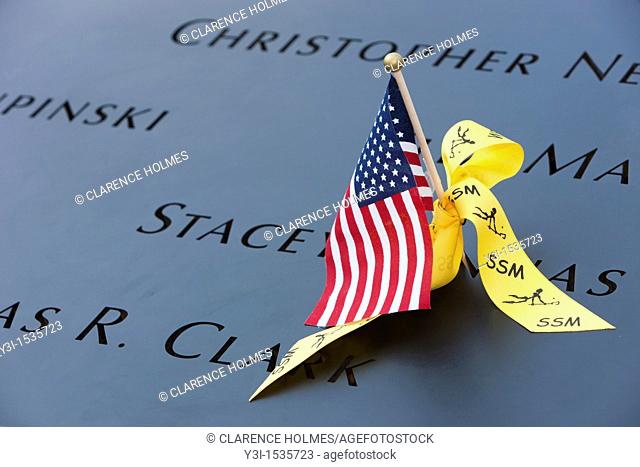 A small American flag and a yellow ribbon left on the names inscribed in the perimeter of one of the pools at the National September 11 Memorial in New York...