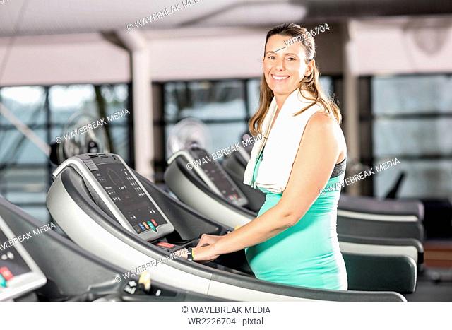 Smiling pregnant woman using treadmill