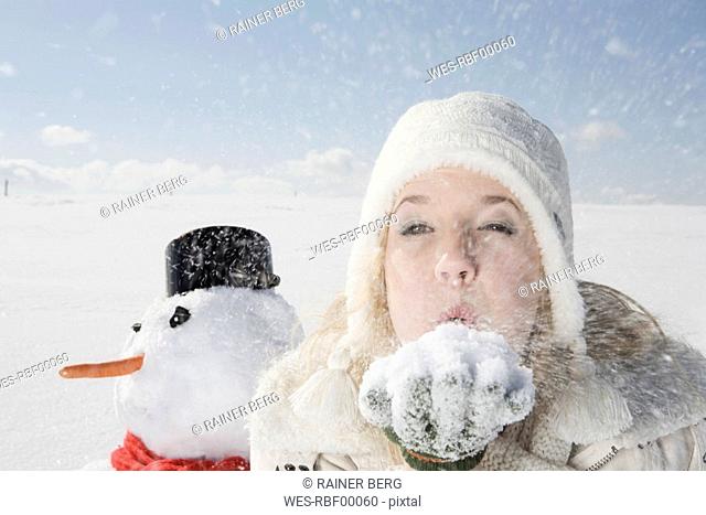Germany, Bavaria, Munich, Young woman blowing snow off hand, portrait