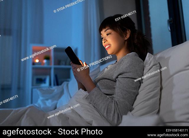 asian woman with smartphone in bed at night