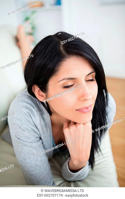 Woman closing her eys as she holds her head with her fist on a couch in a living room