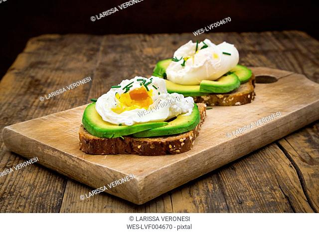 Wholemeal bread slices with sliced avocado and poached eggs on wooden board