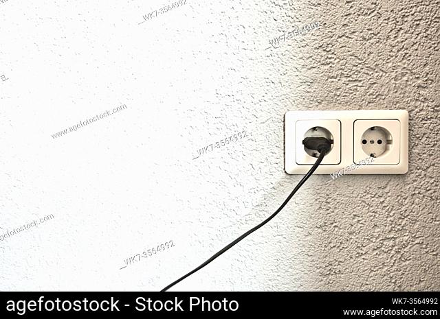 Double electrical power European socket with black cable and plug on white wall space for text close to