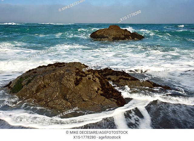 Waves flow over and around large boulders on a California beach