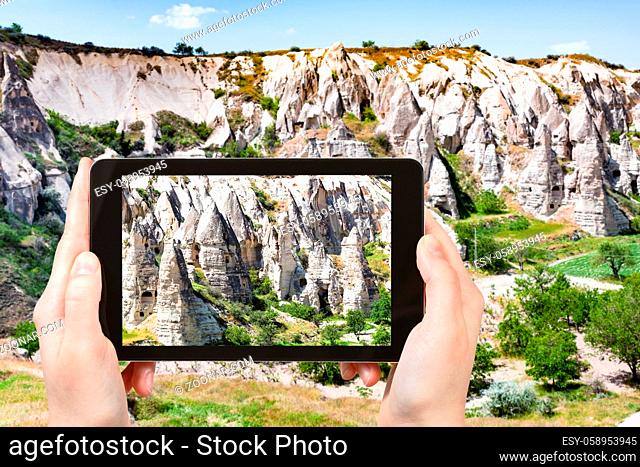 travel concept - tourist photographs of rural landscape with ancient cave churches near Goreme town in Cappadocia on smartphone in Turkey in spring
