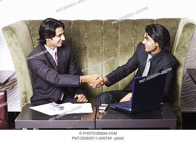 Two businessmen sitting on a couch and shaking hands