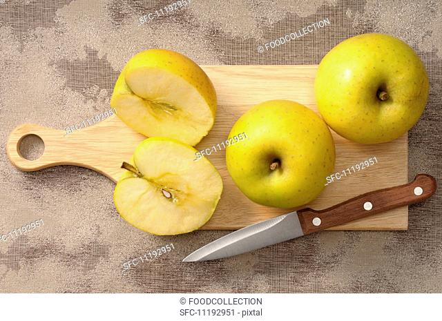 Golden Delicious apples, whole and halved, on a chopping board