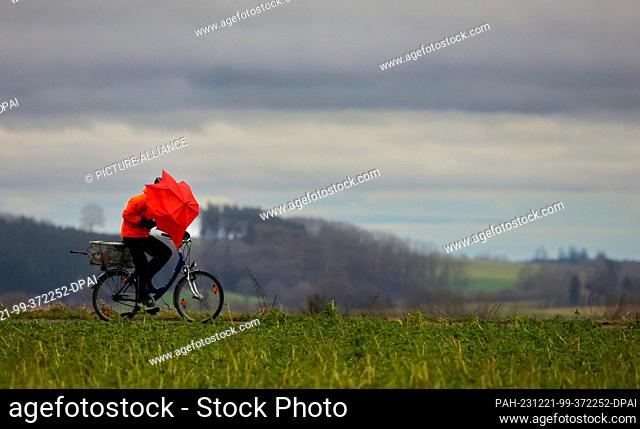 21 December 2023, Baden-Württemberg, Riedlingen: A cyclist is out and about with an umbrella in the rain and storm Photo: Thomas Warnack/dpa