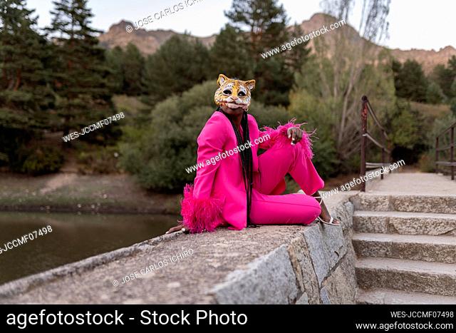 Young woman wearing tiger mask sitting on wall