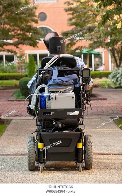 Rear view of a man with Duchenne muscular dystrophy in a motorized wheelchair on the street