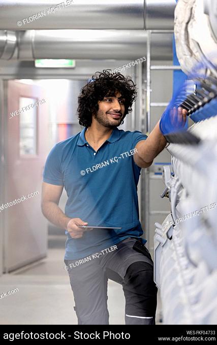 Smiling technician holding tablet PC analyzing machine in factory