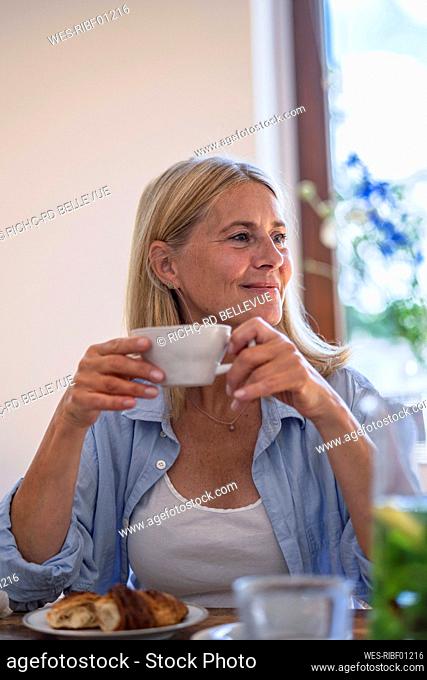 Smiling mature woman holding cup of coffee at home