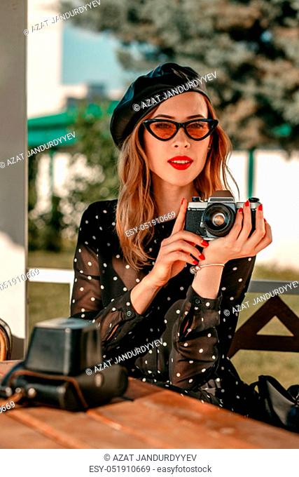 a young woman in a vintage black polka-dot dress with an old camera in her hands posing on the street