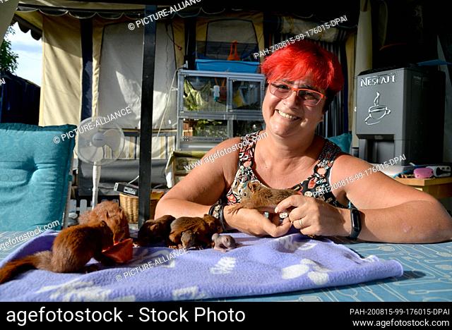12 August 2020, France, Rémering-Les-Puttelange: Squirrel nurse Monika Pfister smiles as young squirrels eat a watermelon on the table in front of her