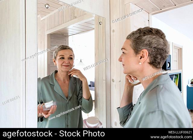 Mature woman looking in mirror applying face cream