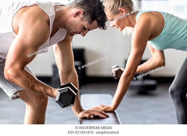 couple exercising with dumbells on a workout bench