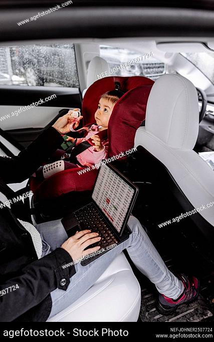 Baby girl sitting in car seat while mother using laptop
