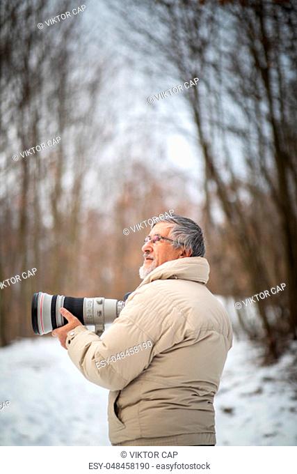 Senior man devoting time to his favorite hobby - photography - taking photos outdoor with his digital camera/DSLR and a big telephoto lens