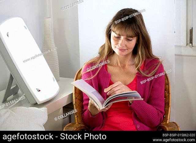 Woman sitting reading near a light therapy lamp