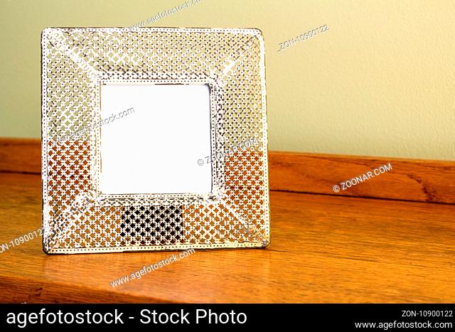 Photo frame - Wide cream coloured metal punched delicate frame with white blank space for image or text standing on oak wood table indoors - background