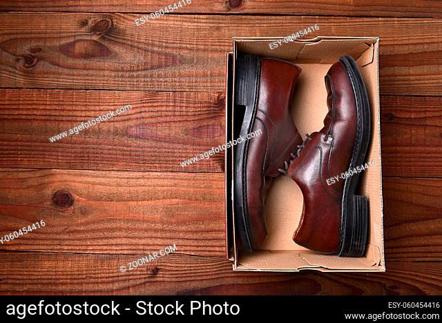 Top view of a pair of mens shoes in a box on a dark wood surface. Horizontal format with copy space