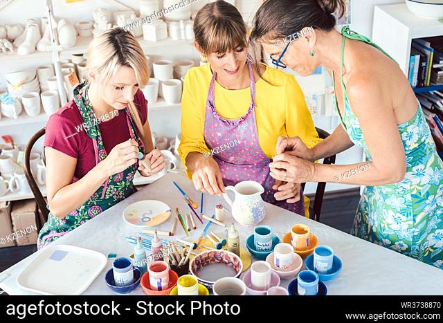 Teacher showing two women in workshop how to paint self-made dishes