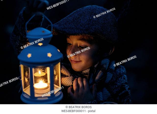 Italy, Grosseto, happy boy looking at lighted Christmas lantern by night