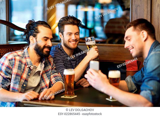 people, men, leisure, friendship and technology concept - happy male friends with smartphone drinking beer at bar or pub