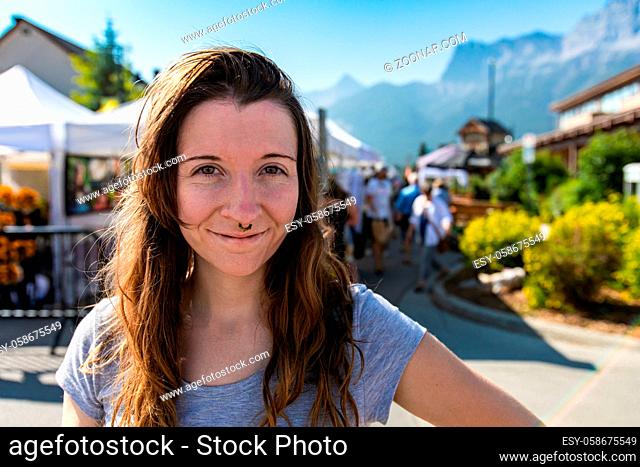 Front portrait of a happy caucasian girl with brown hair and eyes, smiling against a blurred background during a local fair for artisans and traders