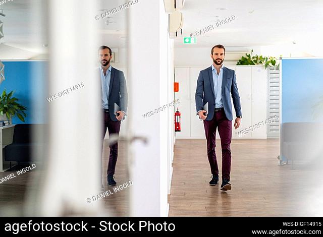 Young businessman walking with digital tablet at office