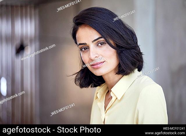 Close-up of businesswoman with black hair against wall in office