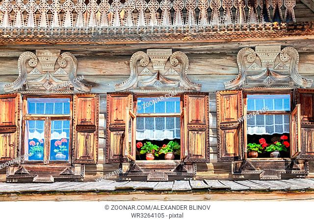 Windows of old traditional Russian log house with carved wooden trim and red geranium flowers