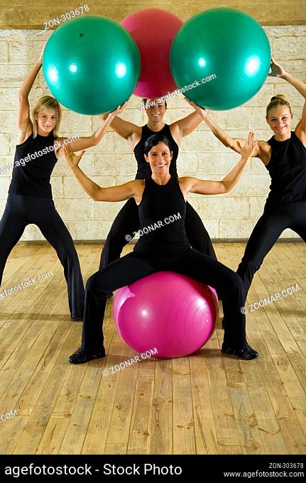 A group of the exercising women posing with big ball. They're smiling and looking at camera. Front view