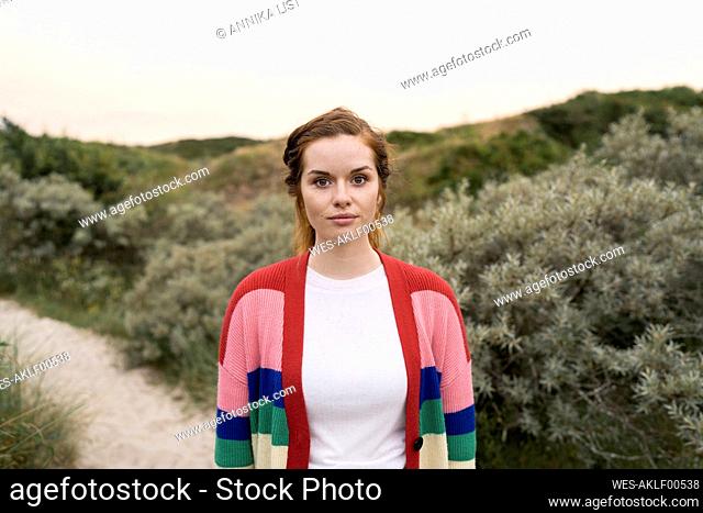Beautiful young woman wearing multi colored cardigan sweater standing in meadow
