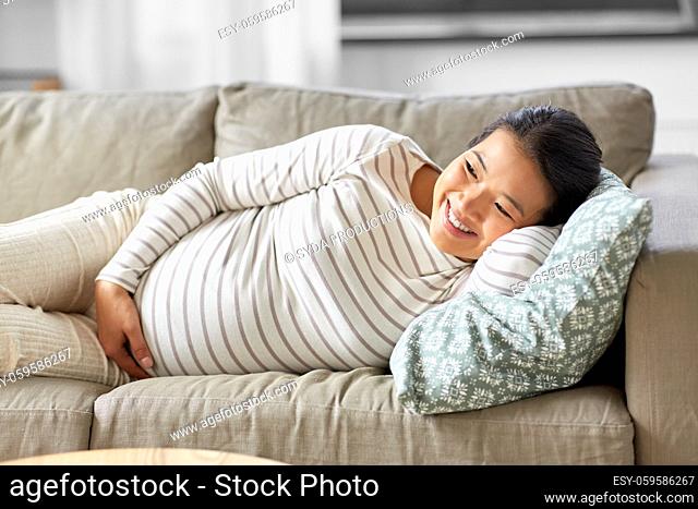 happy pregnant asian woman lying on sofa at home