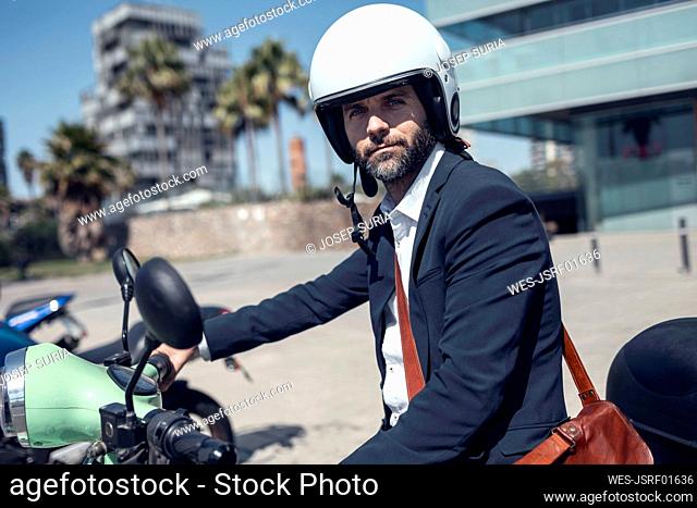Businessman wearing helmet sitting on scooter during sunny day