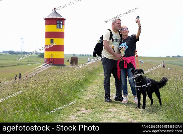05 June 2022, Lower Saxony, Pilsum: A couple takes a selfie at the landmark of Krummhörn. The lighthouse is the landmark of Krummhörn and also known as Otto...